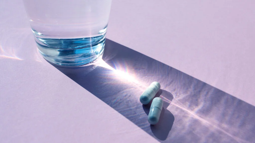5-HTP supplements next to a glass of water in shadow of water on flat surface.