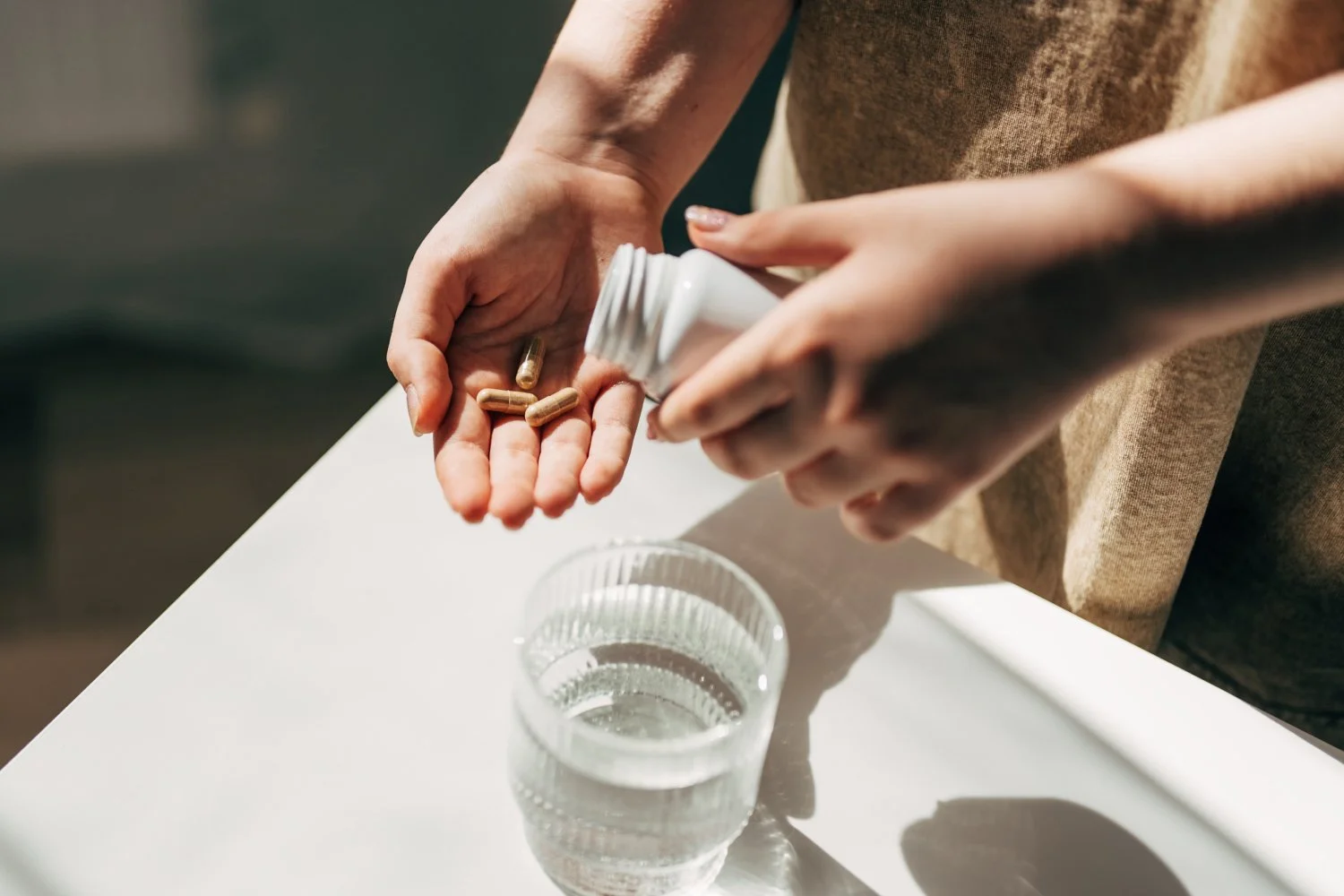 Main tenant une gélule de complément alimentaire bronzage avec un verre d'eau