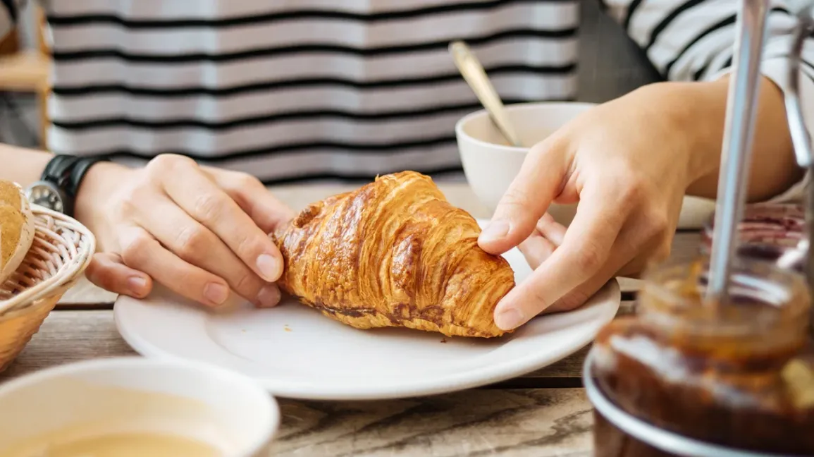 Une personne s'apprêtant à manger un croissant au blé contenant du gluten