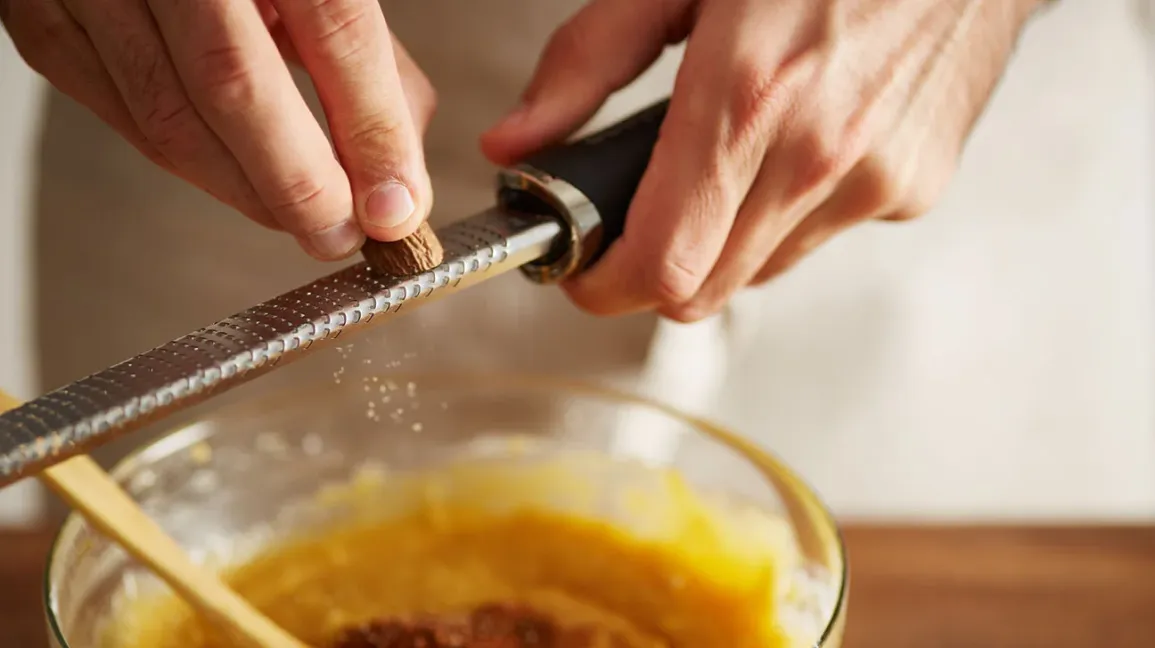 Un homme râpant de la noix de muscade fraîche au-dessus d'un bol